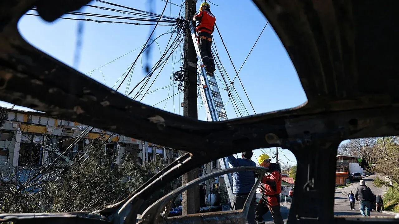 Utility workers fixing power lines viewed through wrecked vehicle in Ukraine.