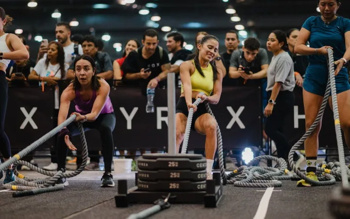 Women pull weighted sledges at a Hyrox competition.