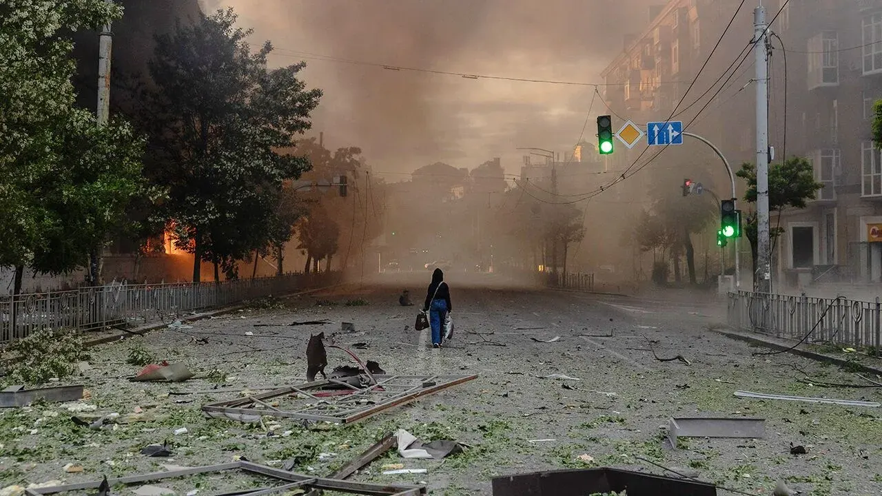Woman walking past war-damaged buildings on smoky Kyiv street after Russian strikes