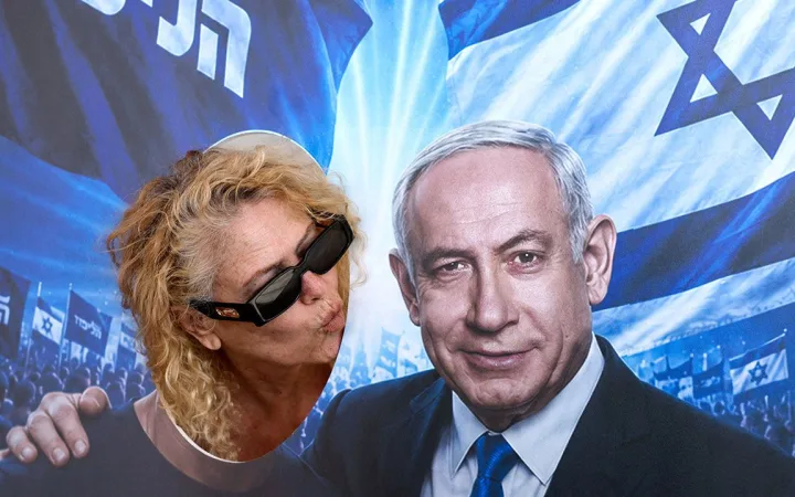 A woman poses in a face-in-the-hole picture cutout, blowing a kiss towards a depiction of Israeli Prime Minister Benjamin Netanyahu