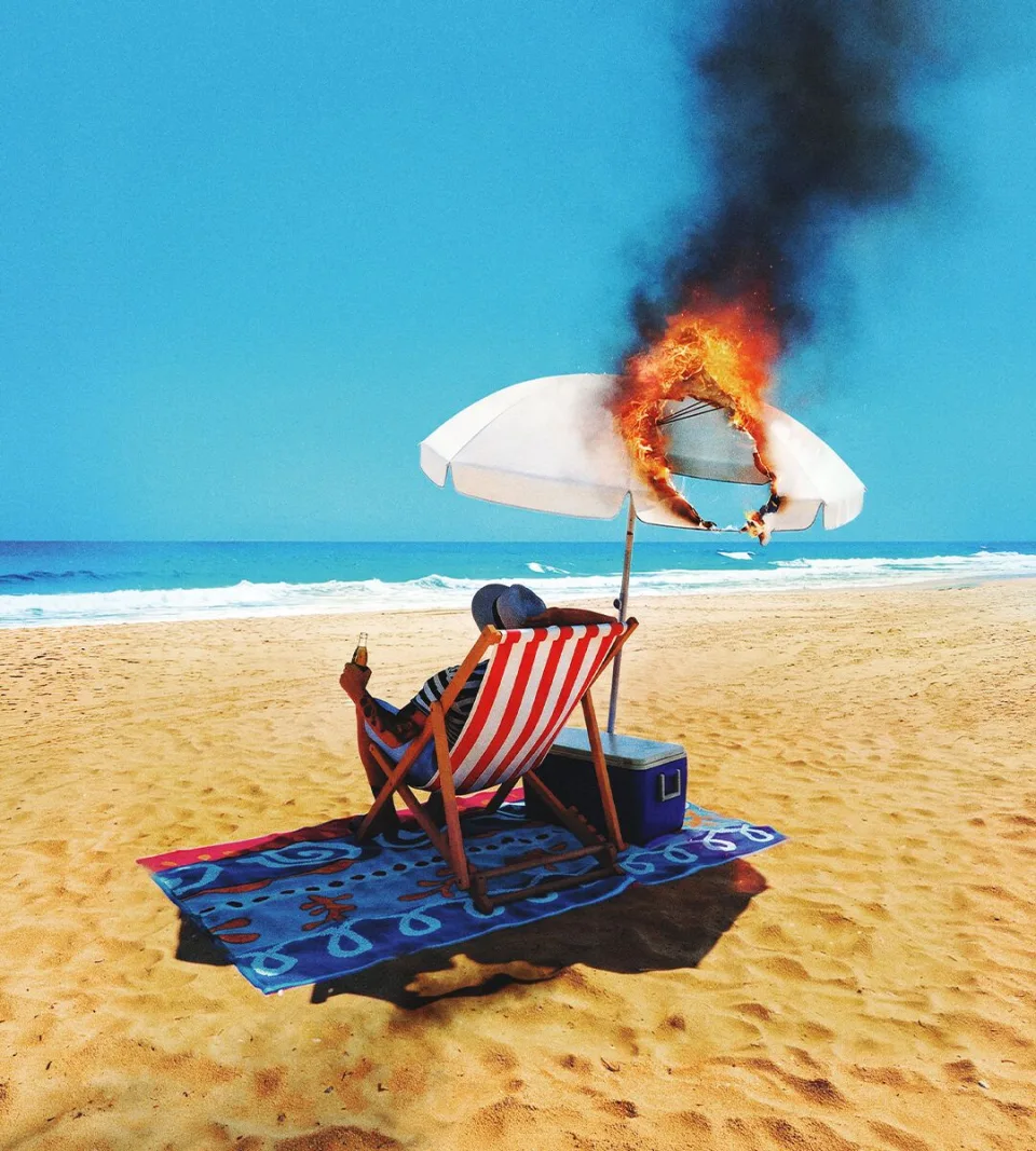 Person relaxing in a deckchair on a beach as the parasol above burns fiercely.