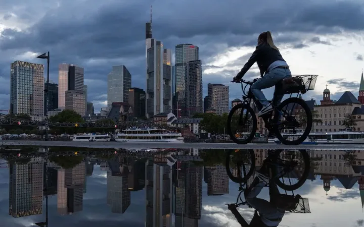 Cyclist passing a puddle mirroring Frankfurt's banking towers after rain