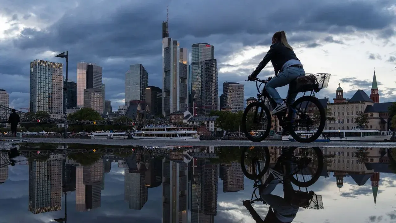 Cyclist passing a puddle mirroring Frankfurt's banking towers after rain