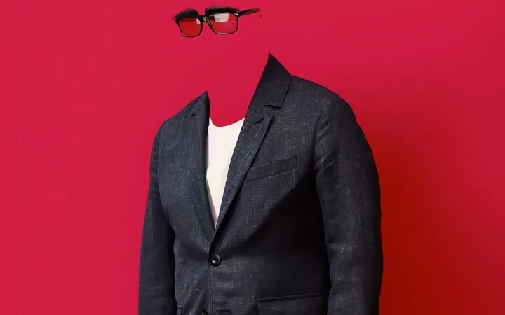A figure in a grey blazer blends into a red background, their face nearly invisible, suggesting anonymity.