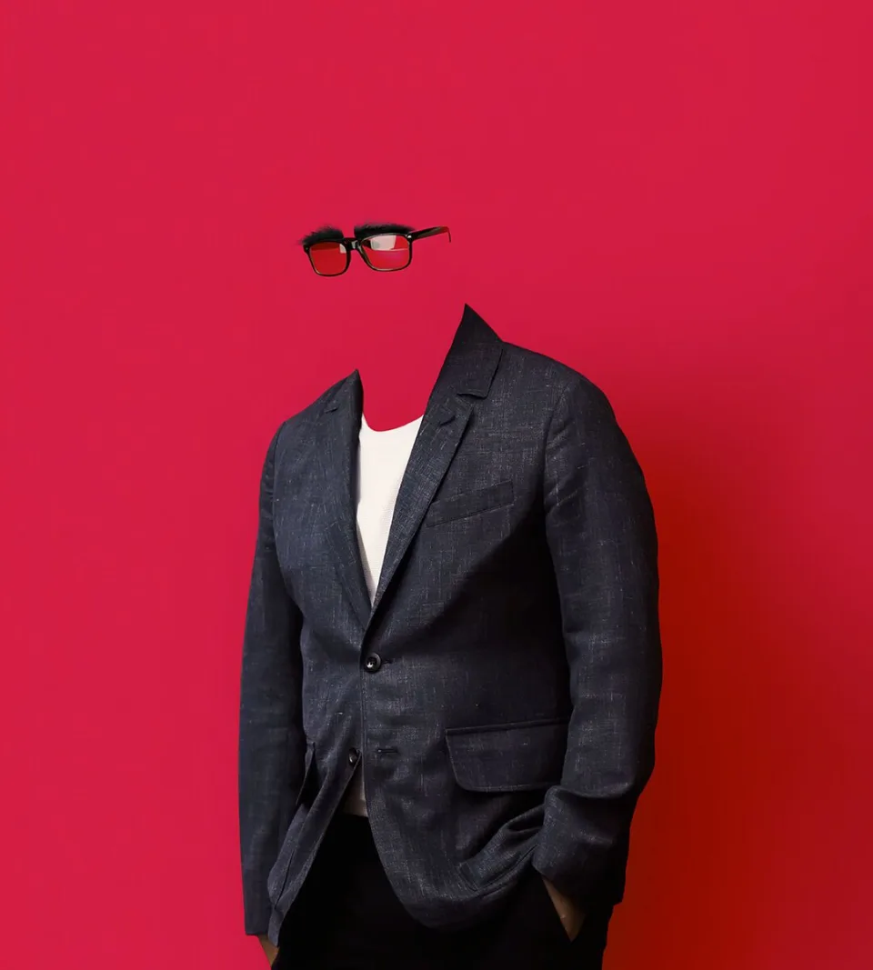 A figure in a grey blazer blends into a red background, their face nearly invisible, suggesting anonymity.
