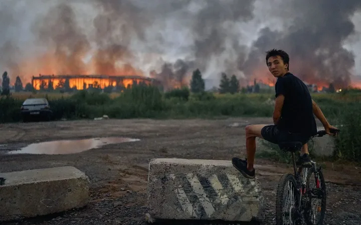 Teenager on bicycle watching smoke and flames from warehouse hit by Russian missile near Kyiv