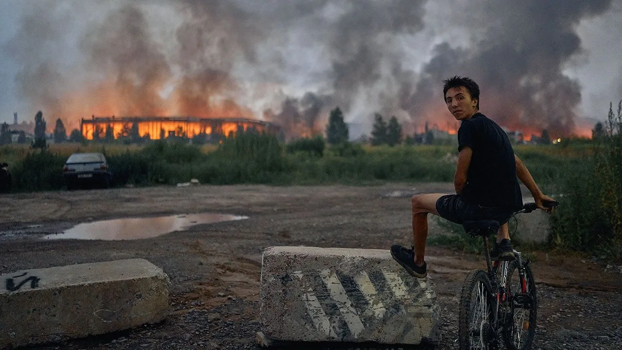 Teenager on bicycle watching smoke and flames from warehouse hit by Russian missile near Kyiv