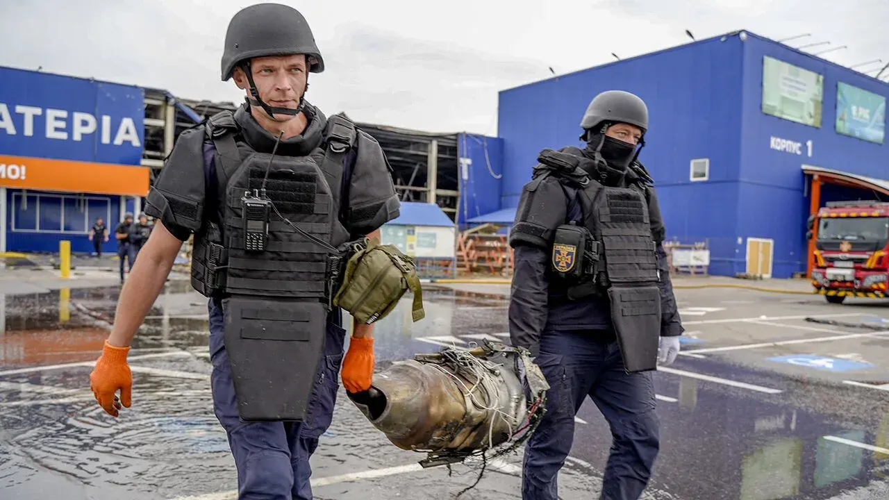 Two armed officers in tactical gear carry an object outside a large retail store.