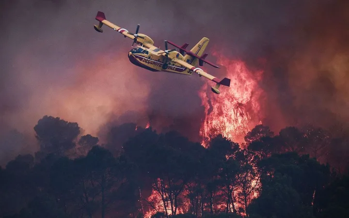 A French Civil Security Canadair CL-415 aircraft flies past flames burning a forest outside Cotignac, France on July 23rd 2026
