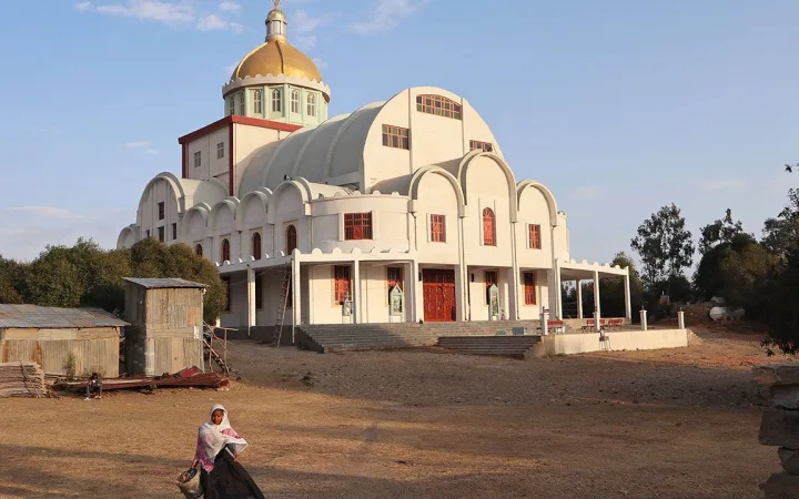 White Orthodox church with a golden dome, a person sits on the ground in front.