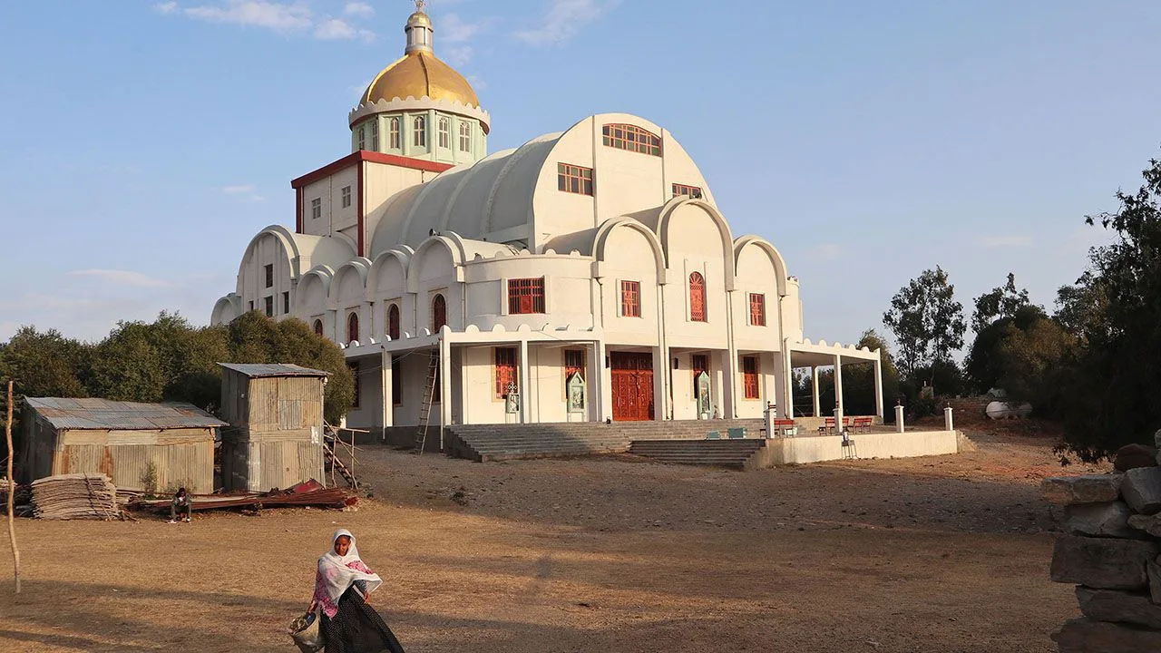 White Orthodox church with a golden dome, a person sits on the ground in front