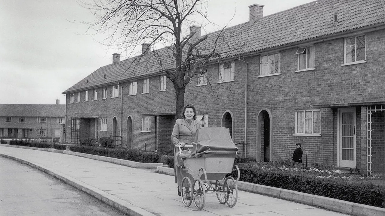 A woman pushing a pram past a row of low-rise council houses on a grey day in Adeyfield, Hemel Hempstead, Hertfordshire