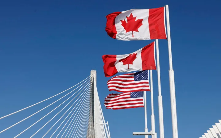 Flags of Canada and the United States fly across the international border on the Gordie Howe International Bridge connecting Windsor, Ontario, and Detroit, Michigan.