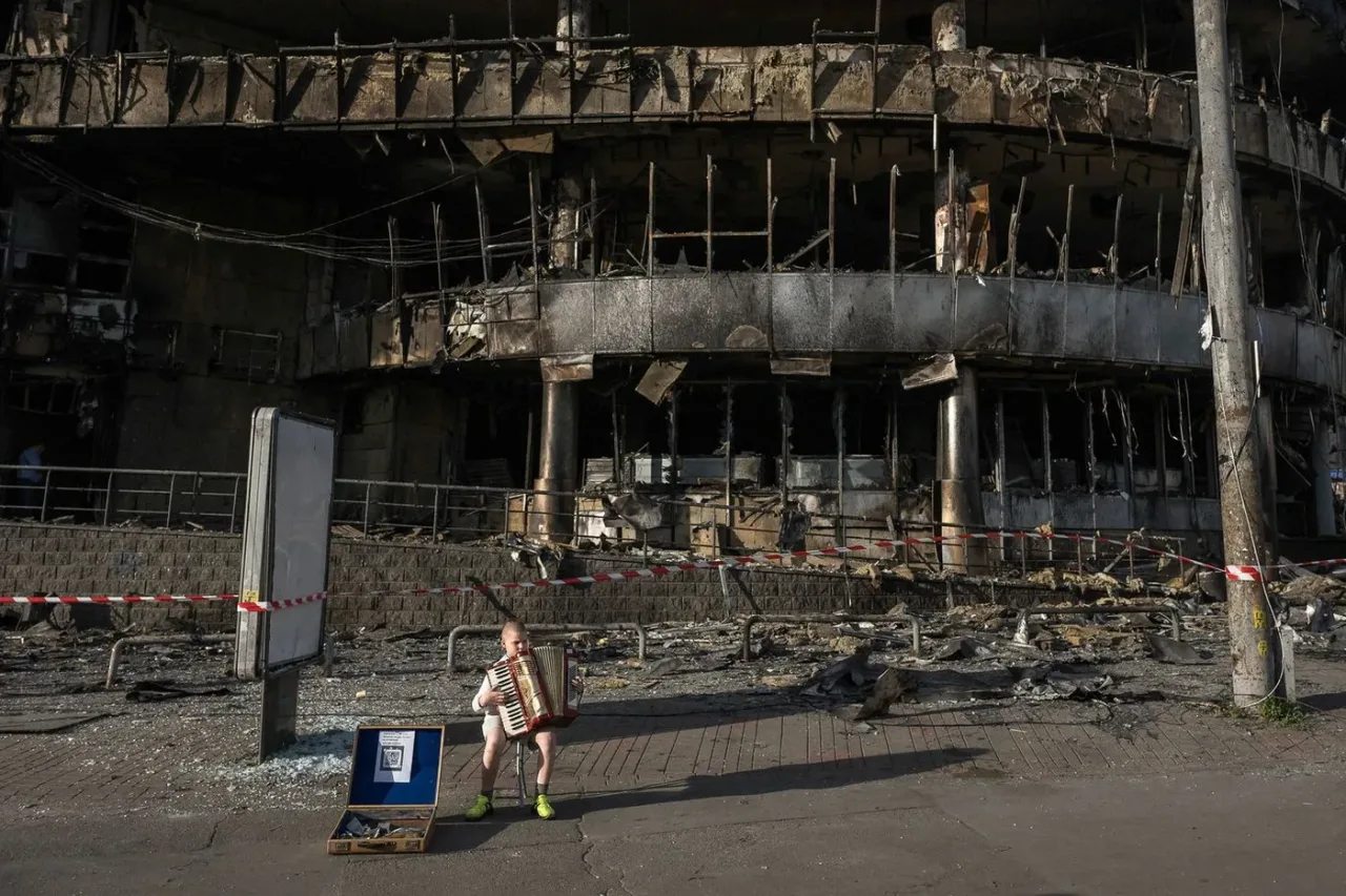 A boy plays the accordion in front of a shopping center damaged by Russian strikes in Kyiv.