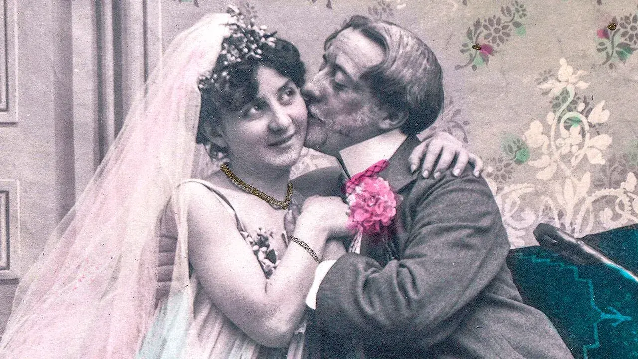 Vintage hand-tinted photograph of a bride and groom sharing a kiss on their wedding day.