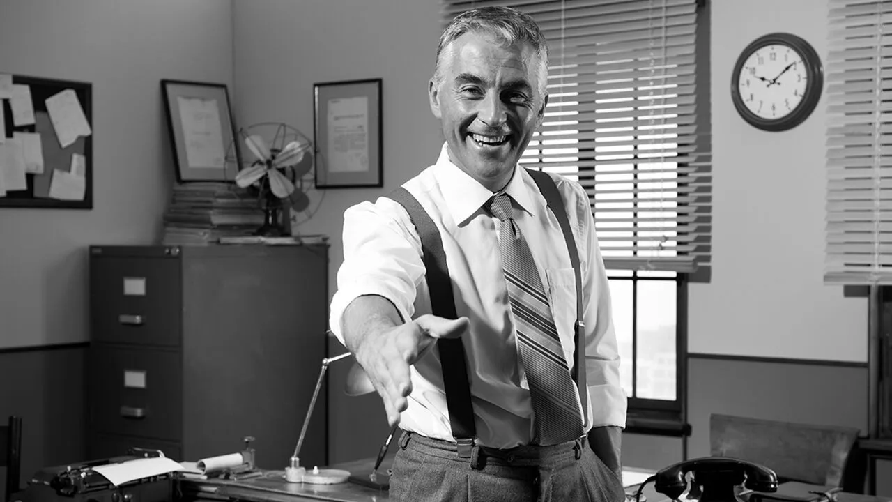A smiling businessman offering a handshake in his office