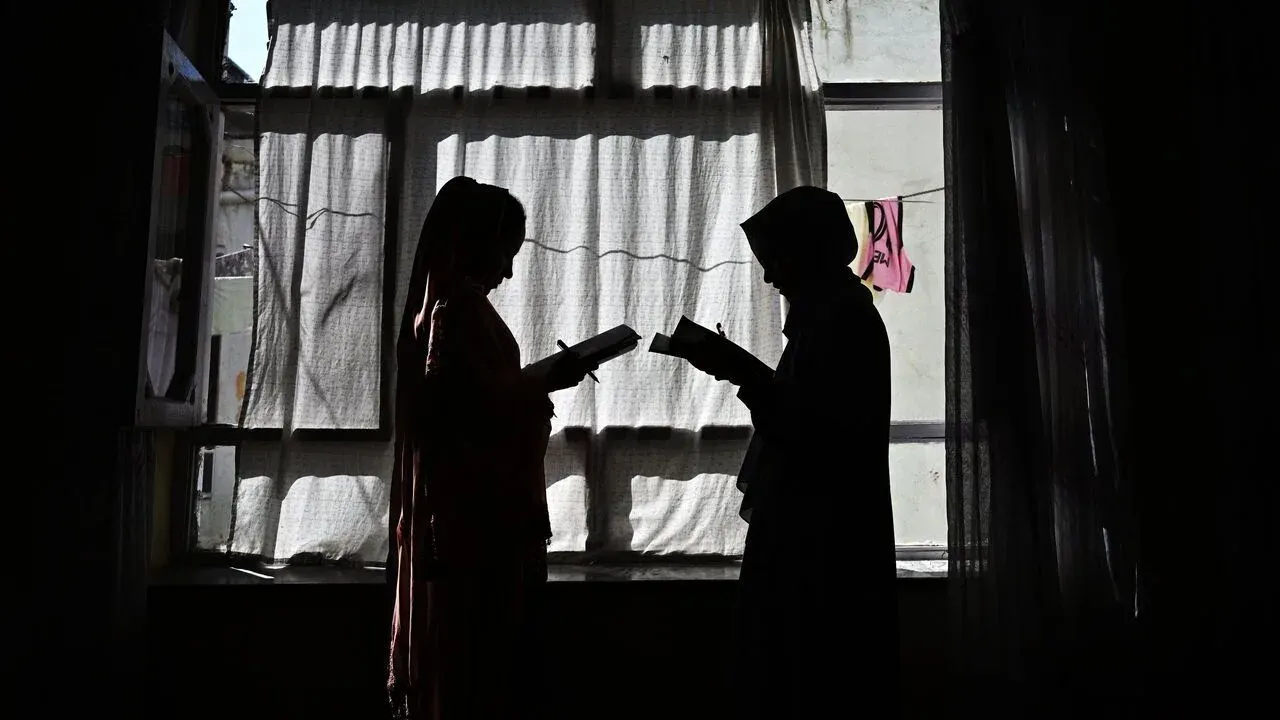 Two children's silhouettes exchanging an object by a window, backlit by natural light.