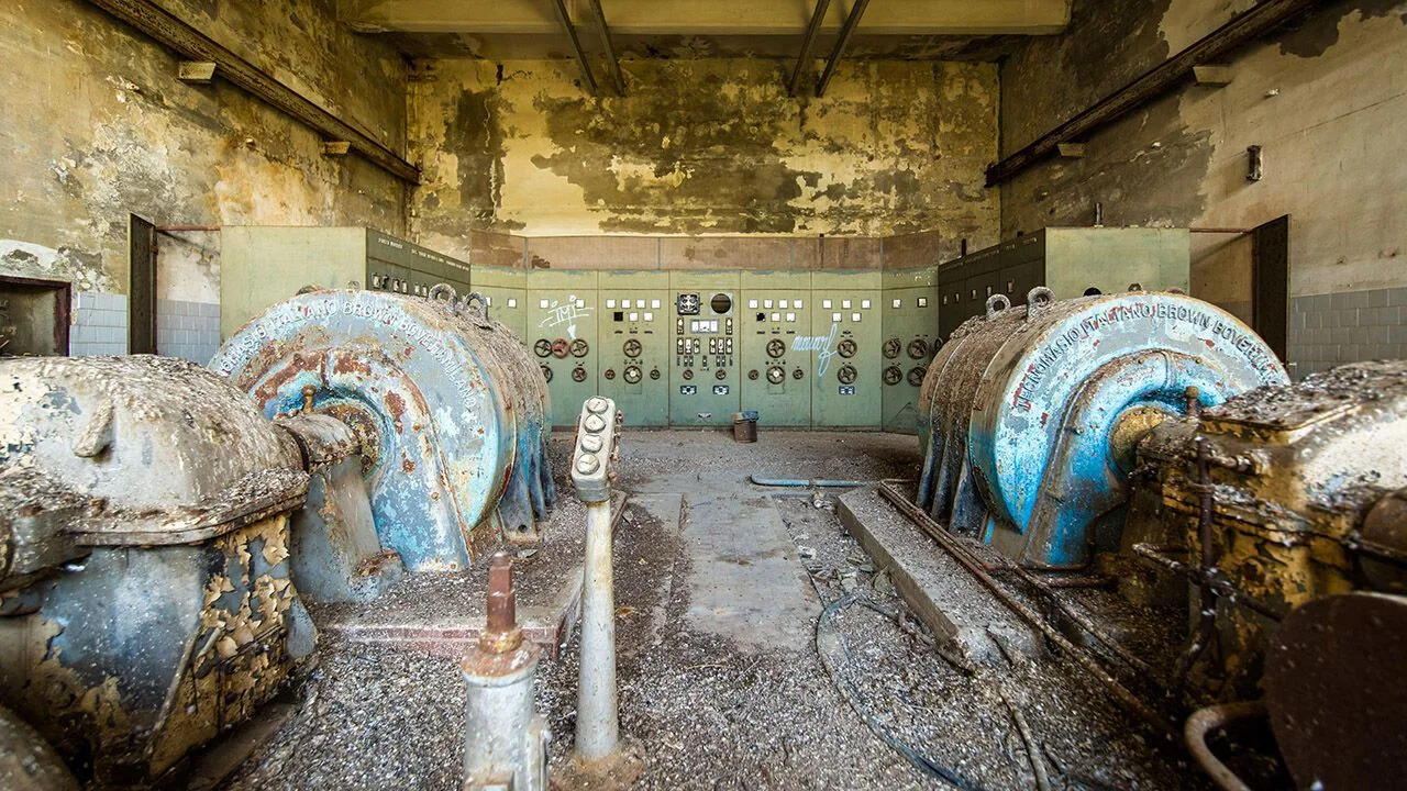 Derelict power station control room with rusty turbines, peeling paint and vintage industrial panels