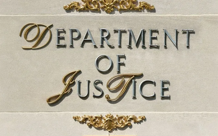 Gold "Department of Justice" lettering on a stone wall in Washington, DC.