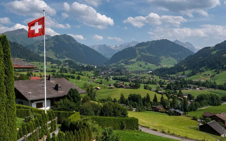 Swiss flag and the Alps surrounding the resort of Gstaad in Saanen municipality, July 23, 2023.