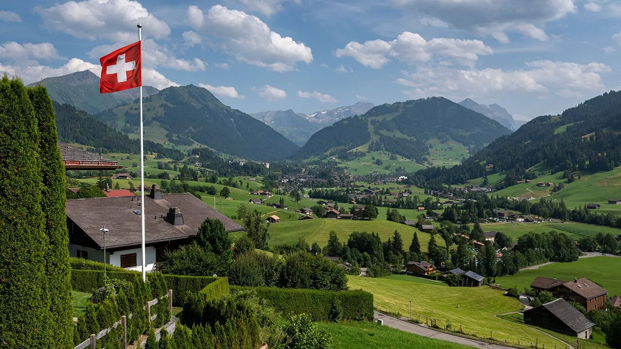 Swiss flag flying above the Alps surrounding the resort of Gstaad in Saanen municipality