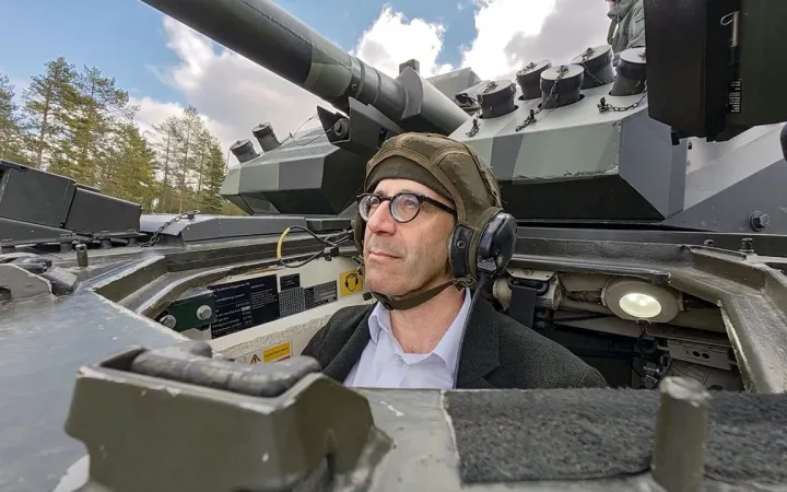 Driver with headset inside an armoured fighting vehicle turret with trees behind