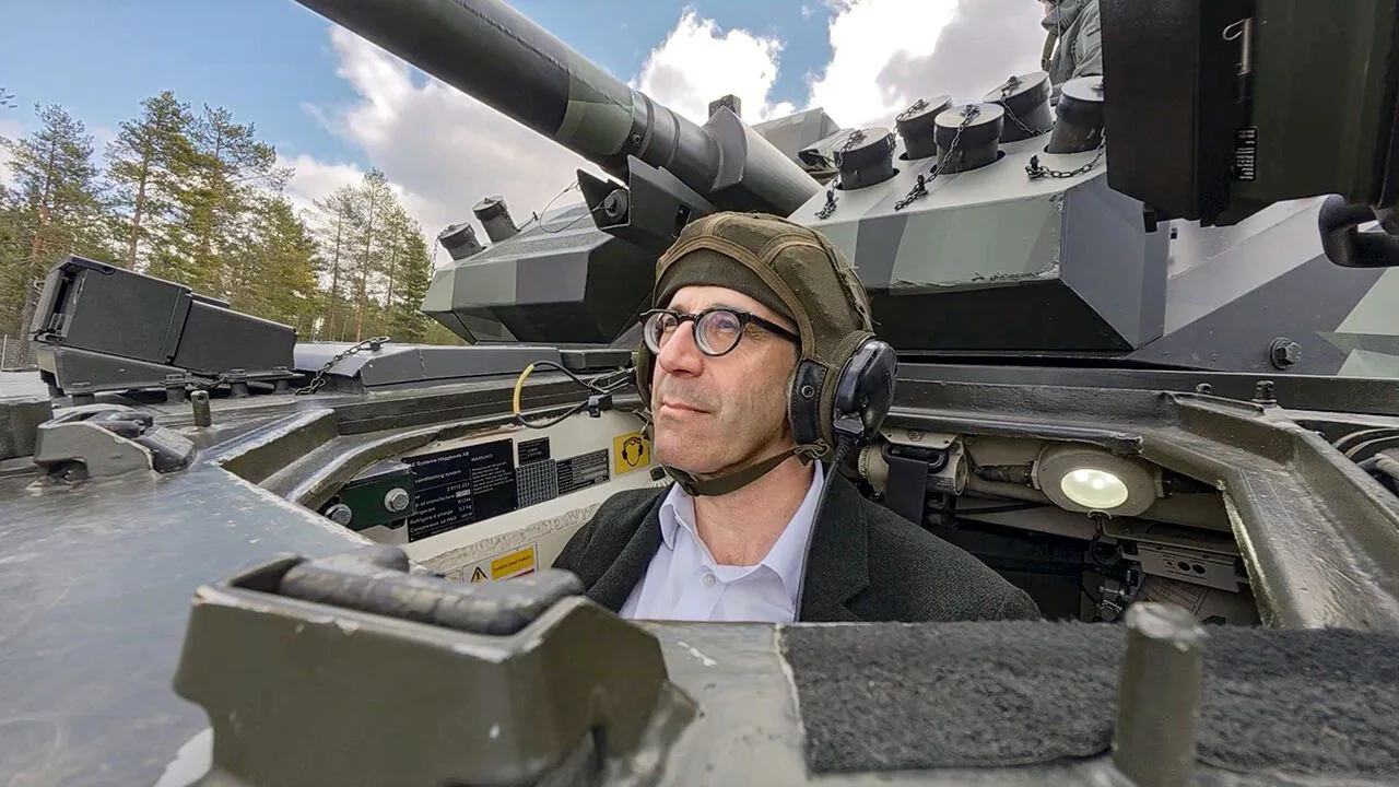 Inside the turret of a CV90 infantry fighting vehicle showing the driver with headset, with trees along the test track behind