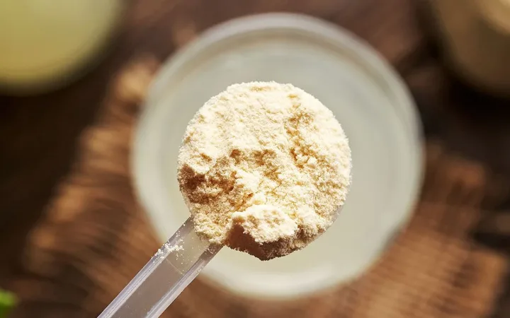 Scoop of whey protein powder beside a shaker bottle