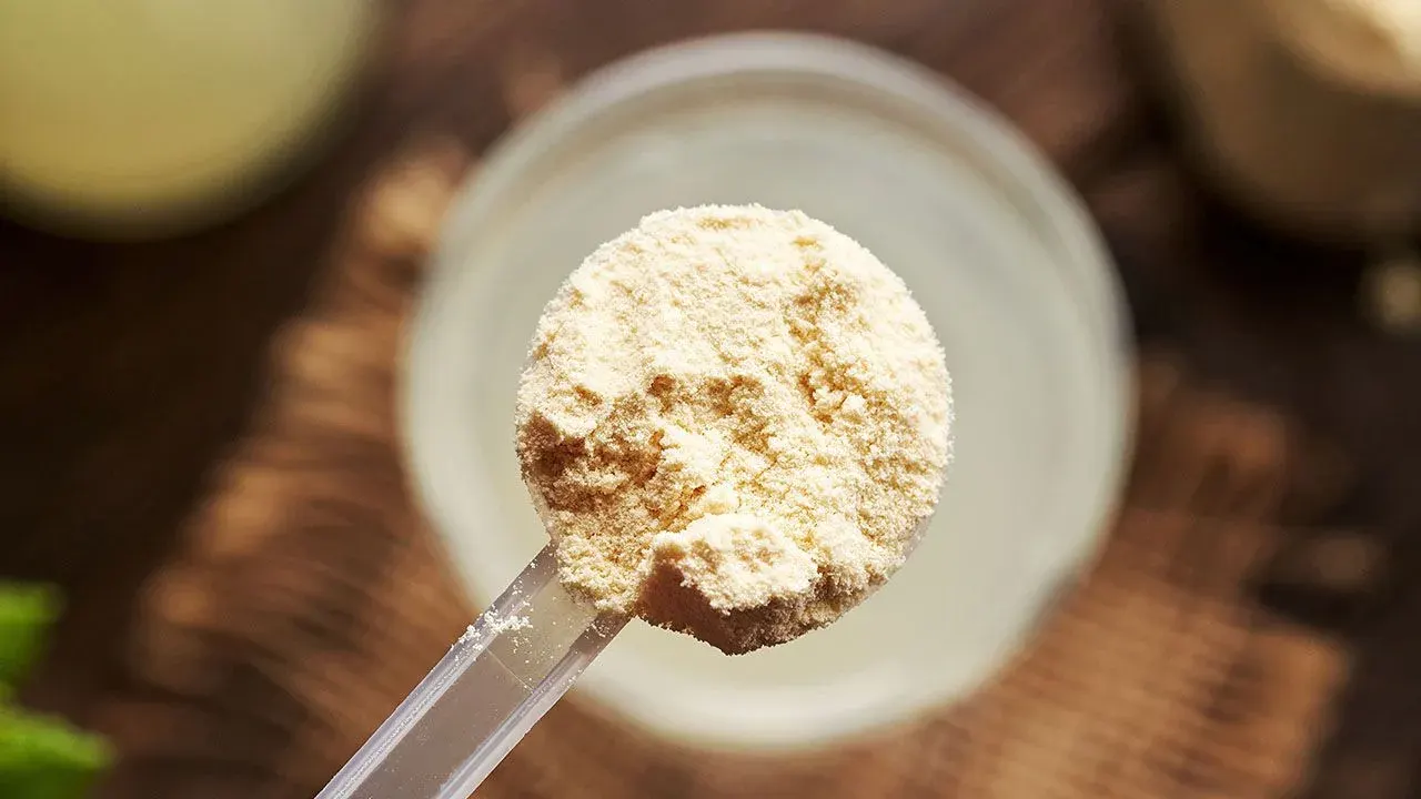 Scoop of whey protein powder beside a shaker bottle