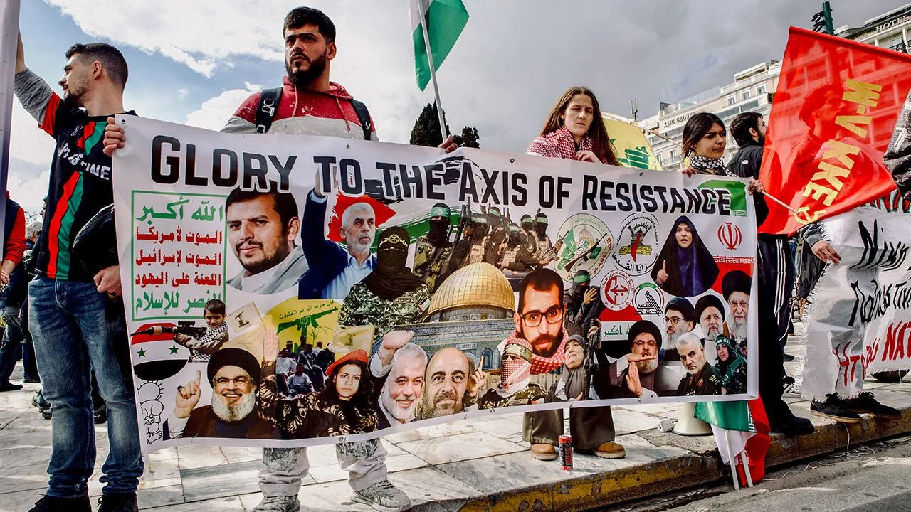 Protesters hold a banner reading Glory to the Axis of Resistance with Palestinian flags raised