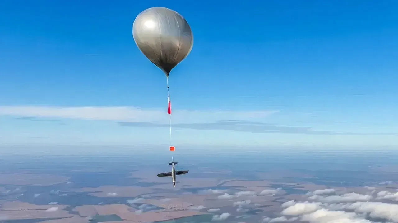 Silvery high-altitude balloon drifting above clouds in clear blue sky.