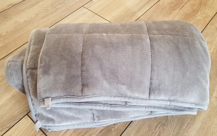 A folded gray weighted blanket on a wooden floor